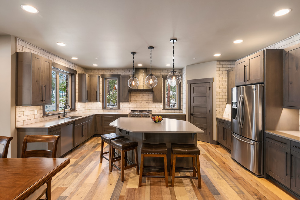 This is an example of a country u-shaped eat-in kitchen in Seattle with an undermount sink, shaker cabinets, brown cabinets, white splashback, subway tile splashback, stainless steel appliances, medium hardwood floors, with island, brown floor and beige benchtop.