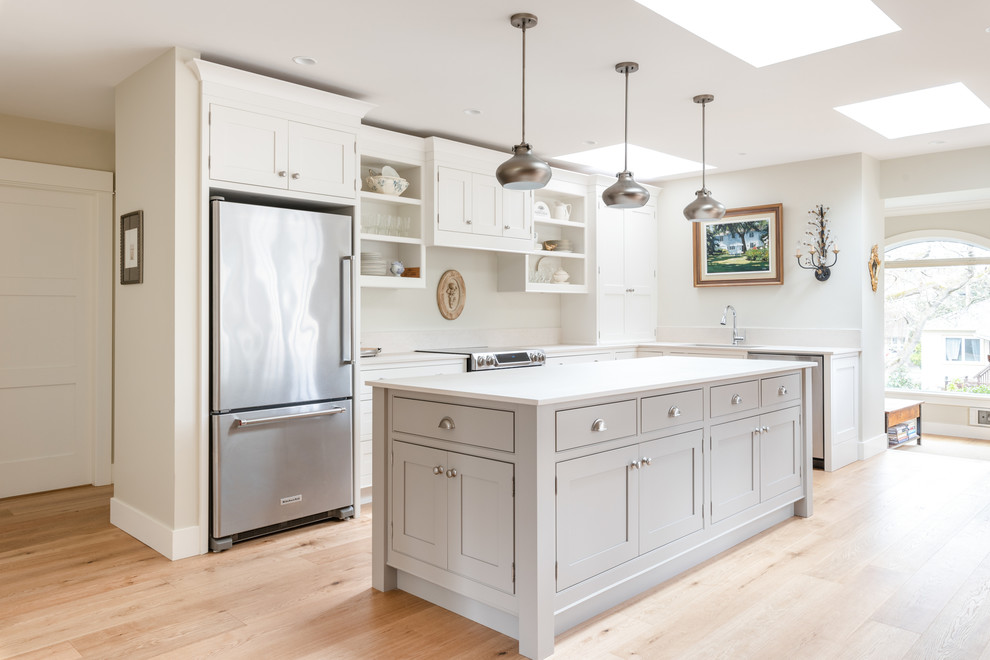 Design ideas for a large traditional l-shaped kitchen in Other with an undermount sink, beaded inset cabinets, white cabinets, solid surface benchtops, stainless steel appliances, light hardwood floors, with island, white benchtop and beige floor.