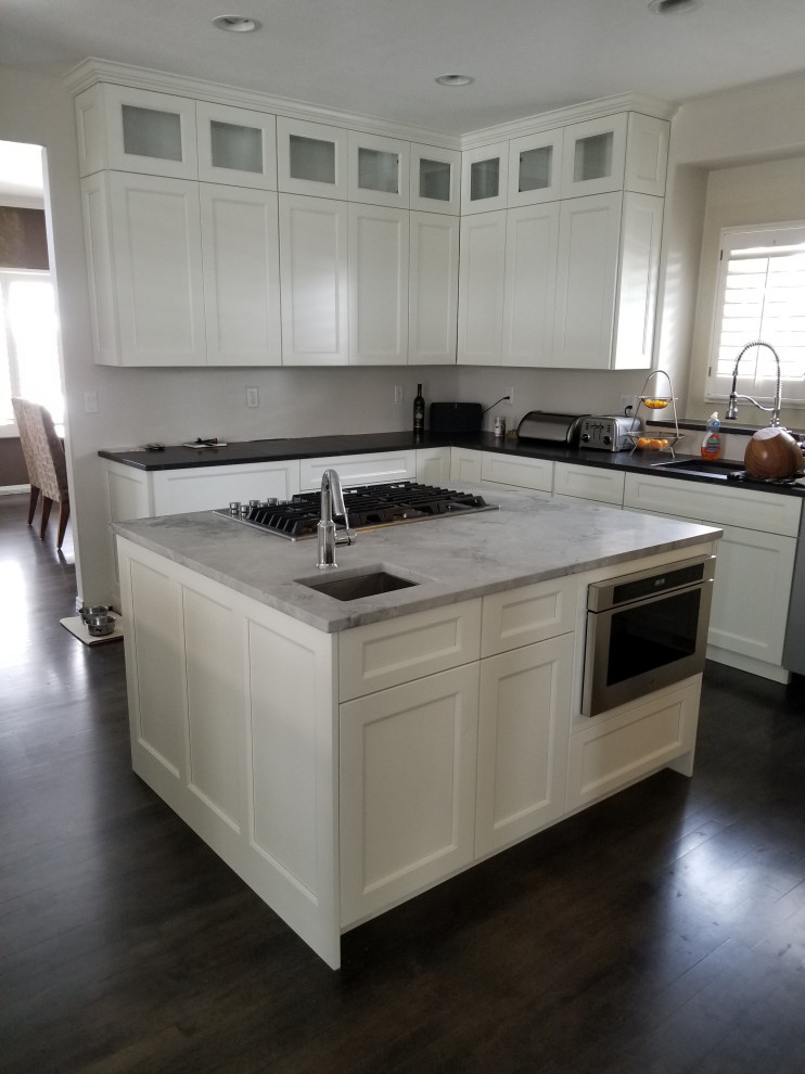 Inspiration for a large transitional u-shaped dark wood floor and brown floor eat-in kitchen remodel in Denver with an undermount sink, shaker cabinets, white cabinets, quartz countertops, stainless steel appliances, an island and black countertops