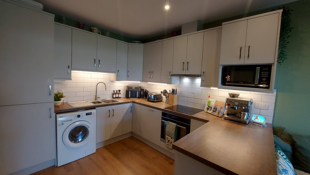 Mid-sized contemporary u-shaped eat-in kitchen in Dublin with a double-bowl sink, flat-panel cabinets, grey cabinets, wood benchtops, white splashback, subway tile splashback, white appliances, laminate floors, no island, brown floor and brown benchtop.