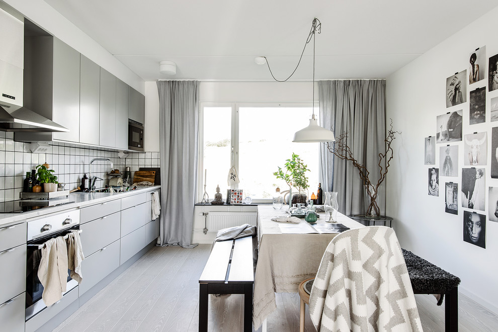 Scandinavian single-wall eat-in kitchen in Stockholm with flat-panel cabinets, grey cabinets, white splashback, stainless steel appliances, light hardwood floors, no island, a single-bowl sink and marble benchtops.