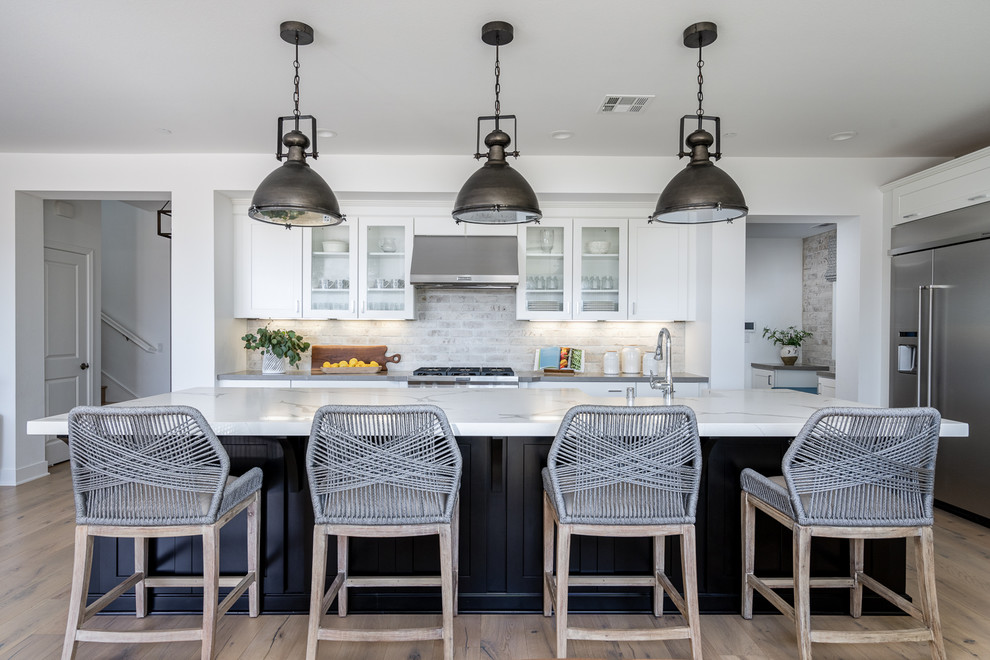 Beach style u-shaped kitchen in Orange County with glass-front cabinets, white cabinets, grey splashback, stainless steel appliances, with island, beige floor and white benchtop.