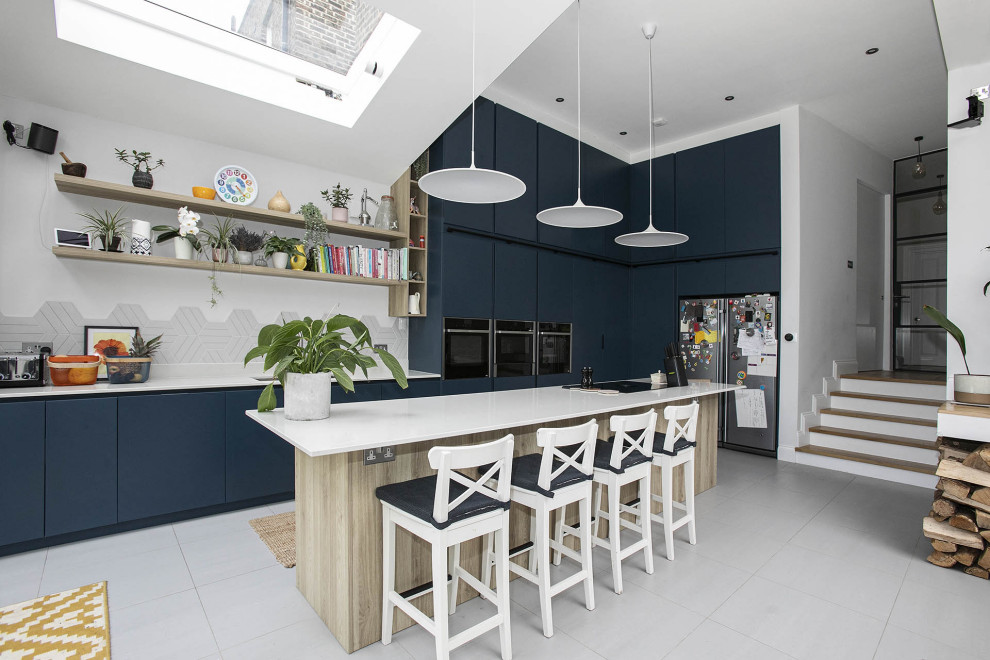 Small contemporary galley open plan kitchen in London with a submerged sink, beaded cabinets, blue cabinets, quartz worktops, white splashback, ceramic splashback, black appliances, ceramic flooring, an island, white floors, white worktops, a vaulted ceiling and feature lighting.