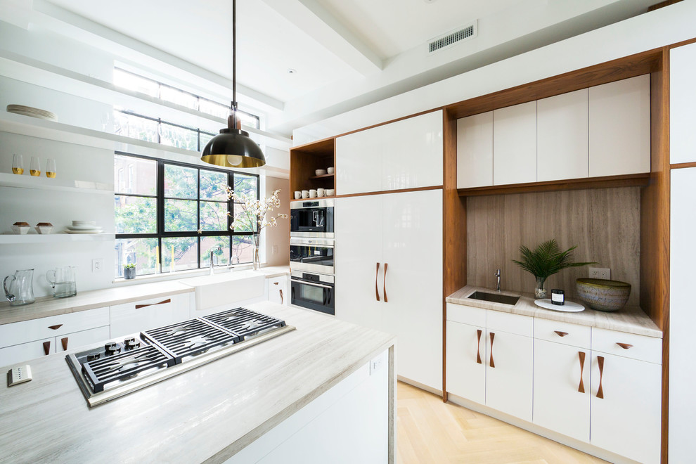 Photo of a mid-sized contemporary u-shaped kitchen in New York with a drop-in sink, flat-panel cabinets, white cabinets, beige splashback, stainless steel appliances, light hardwood floors, with island, beige floor and beige benchtop.