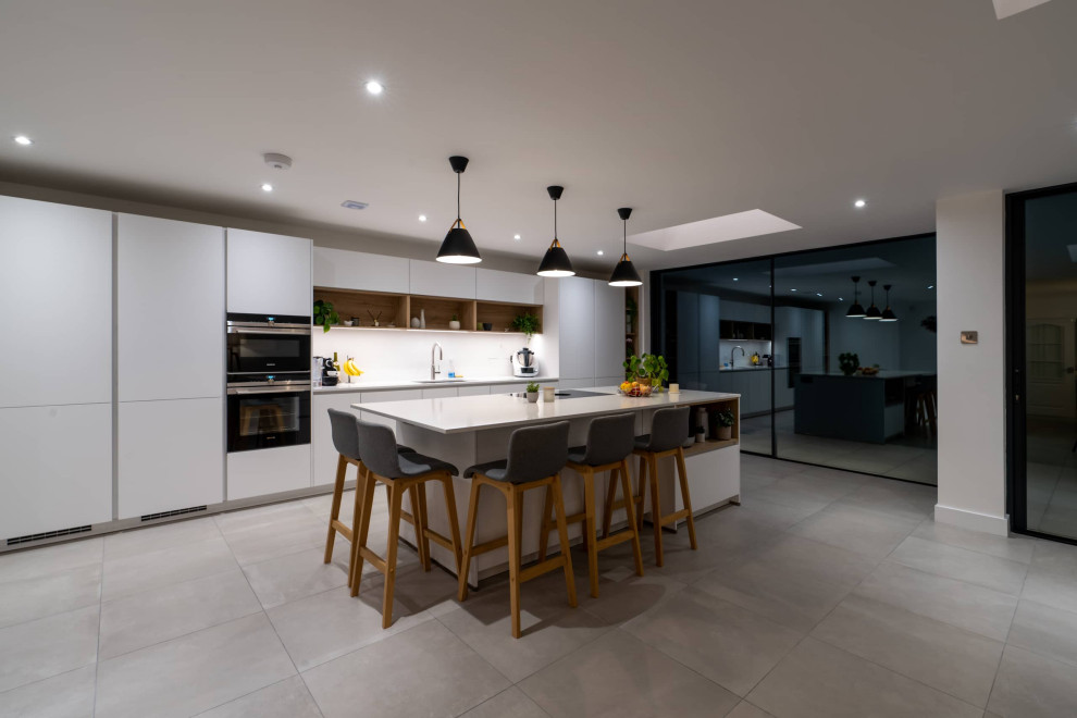 Inspiration for a large scandinavian galley open plan kitchen in Hertfordshire with flat-panel cabinets, white cabinets, quartz worktops, white splashback, black appliances, an island, white floors, white worktops and feature lighting.