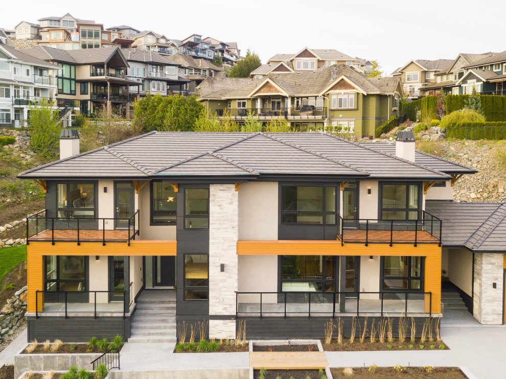 This is an example of a large contemporary three-storey stucco brown house exterior in Vancouver with a flat roof and a tile roof.