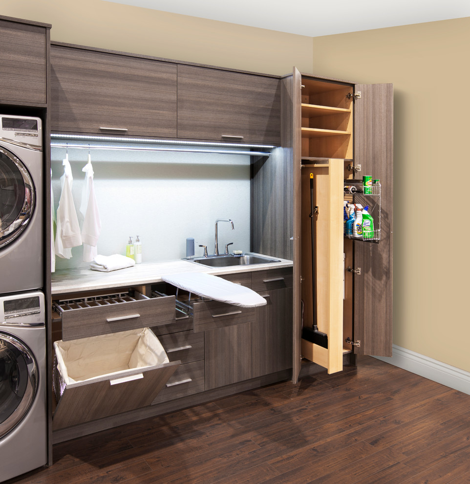 This is an example of a mid-sized contemporary single-wall utility room in Toronto with flat-panel cabinets, beige walls, a stacked washer and dryer and grey cabinets.