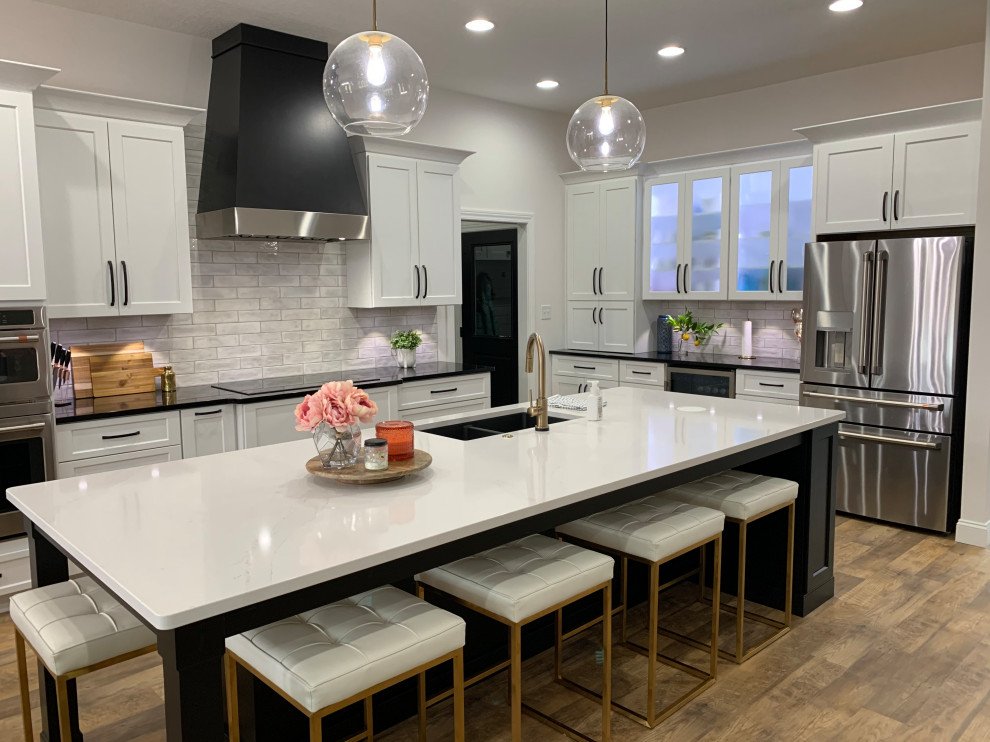 Open concept kitchen - large transitional l-shaped vinyl floor and brown floor open concept kitchen idea with an undermount sink, recessed-panel cabinets, white cabinets, quartz countertops, white backsplash, ceramic backsplash, stainless steel appliances, an island and white countertops