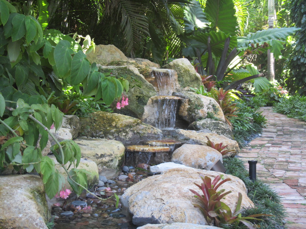 Photo of a large traditional backyard shaded garden in Miami with a water feature and natural stone pavers.