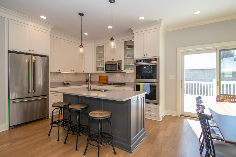 Mid-sized transitional l-shaped eat-in kitchen in Milwaukee with an undermount sink, white cabinets, granite benchtops, white splashback, ceramic splashback, stainless steel appliances, with island, brown floor, grey benchtop, shaker cabinets and light hardwood floors.