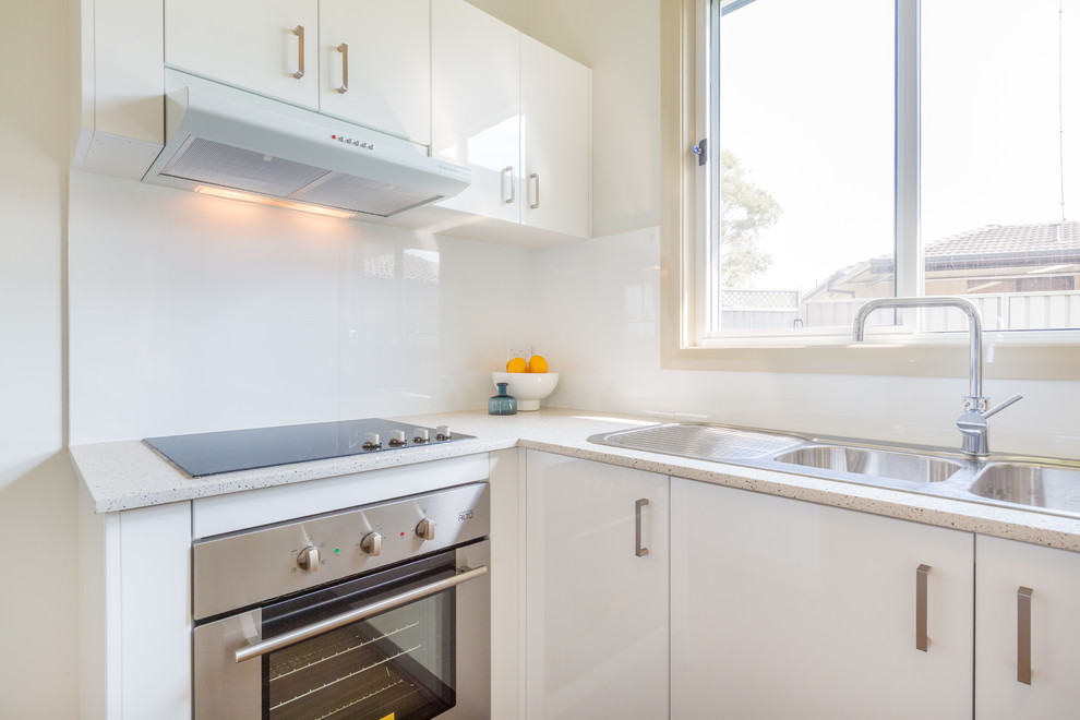 Mid-sized contemporary u-shaped eat-in kitchen in Sydney with a double-bowl sink, white cabinets, granite benchtops, white splashback, ceramic splashback, stainless steel appliances and laminate floors.