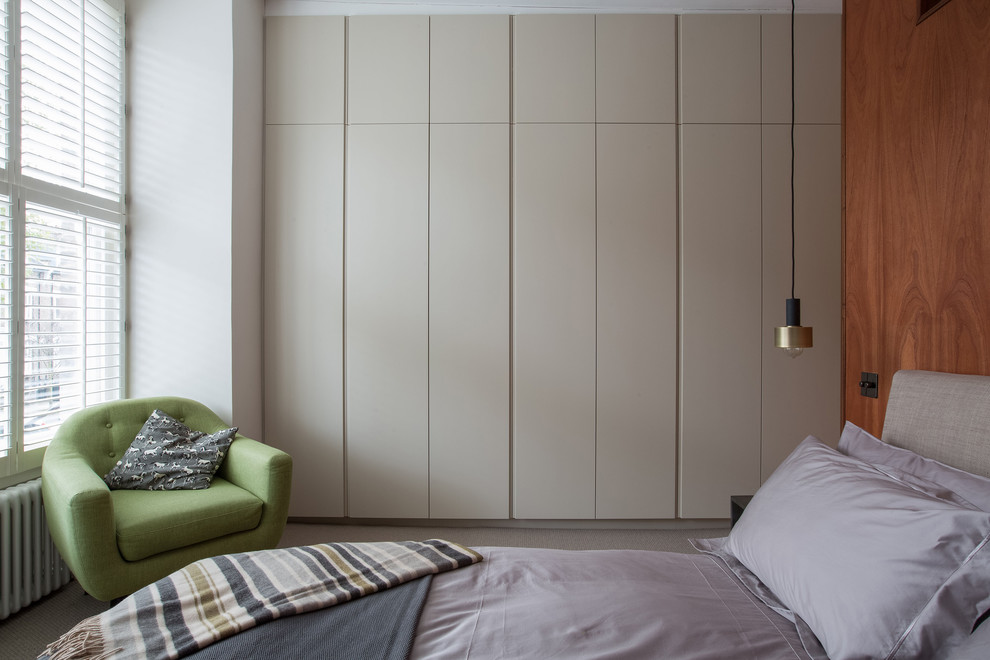 Large eclectic master bedroom in London with beige walls, carpet and beige floor.