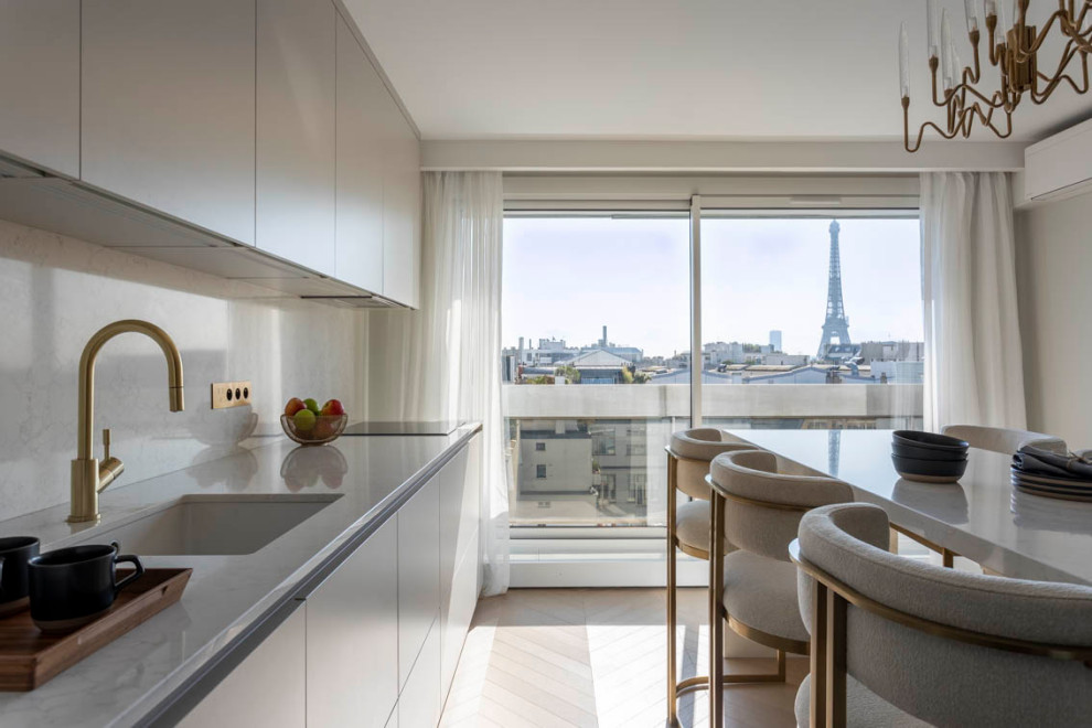Large modern galley open plan kitchen in Paris with an integrated sink, white cabinets, marble benchtops, white splashback, marble splashback, panelled appliances, light hardwood floors, with island and white benchtop.