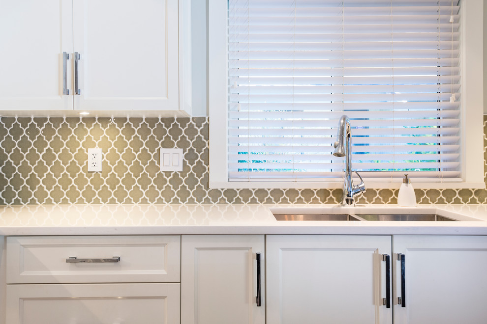 Inspiration for a mid-sized transitional l-shaped medium tone wood floor open concept kitchen remodel in Vancouver with an undermount sink, shaker cabinets, white cabinets, quartz countertops, green backsplash, glass tile backsplash, stainless steel appliances and an island
