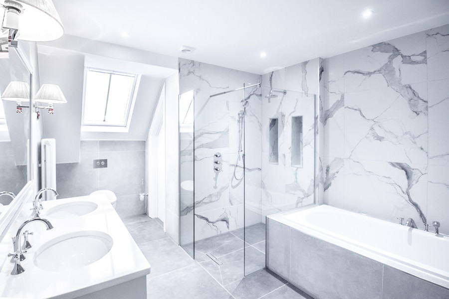 This is an example of a large traditional kids wet room bathroom in London with shaker cabinets, grey cabinets, a drop-in tub, a wall-mount toilet, white tile, marble, grey walls, porcelain floors, an undermount sink, limestone benchtops, grey floor, an open shower, white benchtops, a double vanity, a built-in vanity and vaulted.