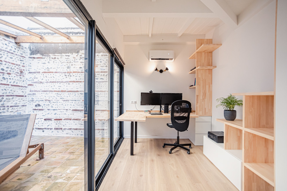 Ejemplo de despacho actual pequeño con paredes blancas, suelo de madera clara, escritorio empotrado y machihembrado