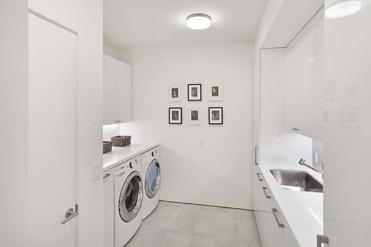 This is an example of a large modern galley dedicated laundry room in San Francisco with an undermount sink, flat-panel cabinets, white cabinets, quartzite benchtops, white walls, porcelain floors and a side-by-side washer and dryer.