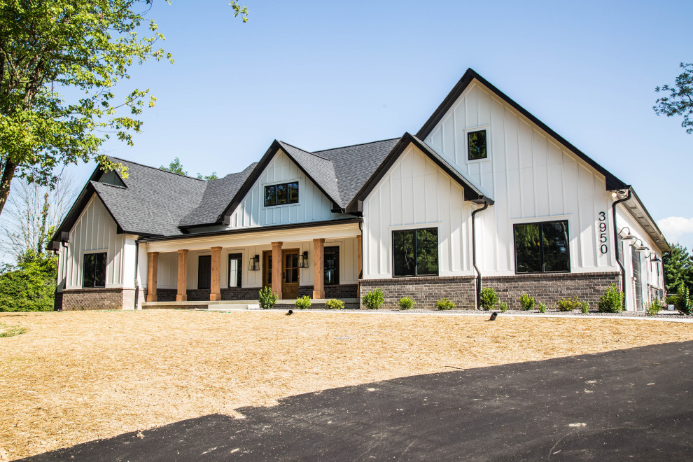 Aménagement d'une grande façade de maison blanche campagne en panneau de béton fibré et planches et couvre-joints de plain-pied avec un toit à deux pans, un toit en shingle et un toit noir.