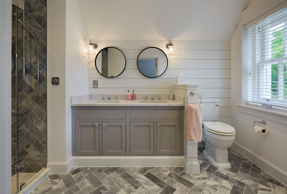 This is an example of a mid-sized beach style master bathroom in Hertfordshire with shaker cabinets, grey cabinets, a two-piece toilet, white walls, marble floors, a drop-in sink, quartzite benchtops, grey floor, a hinged shower door and white benchtops.