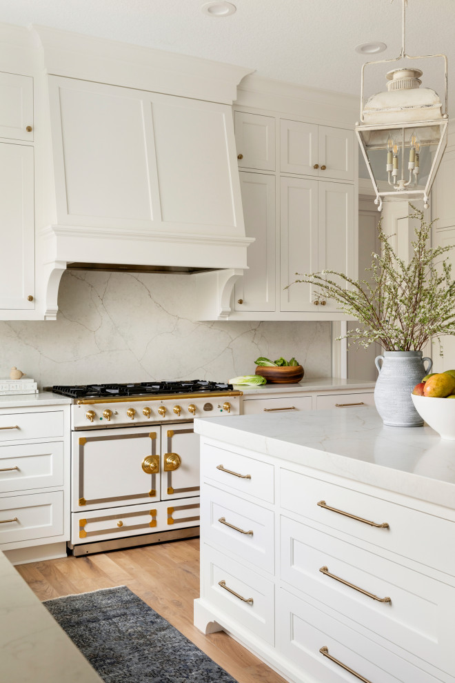 Inspiration for an expansive traditional u-shaped eat-in kitchen in Minneapolis with a farmhouse sink, recessed-panel cabinets, white cabinets, quartz benchtops, white splashback, engineered quartz splashback, white appliances, light hardwood floors, with island, brown floor and white benchtop.