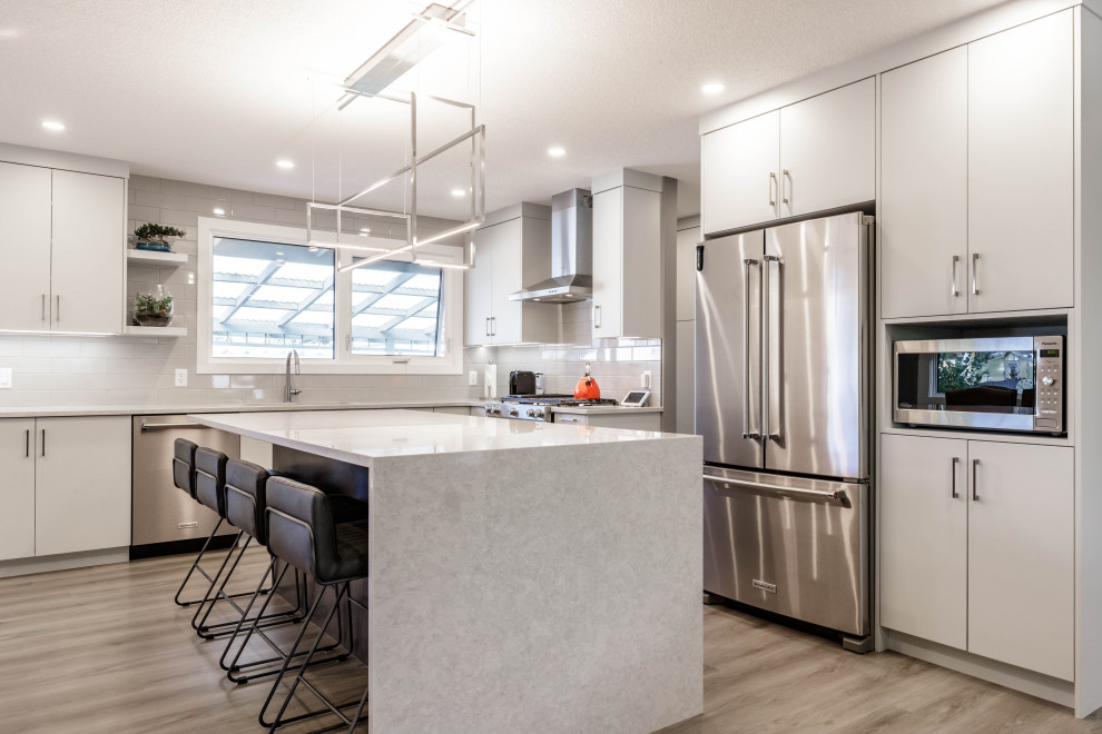 Medium sized contemporary l-shaped open plan kitchen in Calgary with a submerged sink, flat-panel cabinets, white cabinets, engineered stone countertops, white splashback, porcelain splashback, stainless steel appliances, medium hardwood flooring, multiple islands, brown floors, a timber clad ceiling and white worktops.