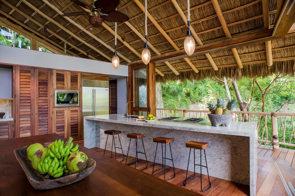 This is an example of a tropical open plan kitchen in Hawaii with louvered cabinets, medium wood cabinets, medium hardwood floors and with island.