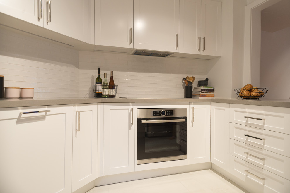 Photo of a small contemporary u-shaped eat-in kitchen in Sydney with a farmhouse sink, shaker cabinets, white cabinets, quartz benchtops, white splashback, ceramic splashback, stainless steel appliances and ceramic floors.