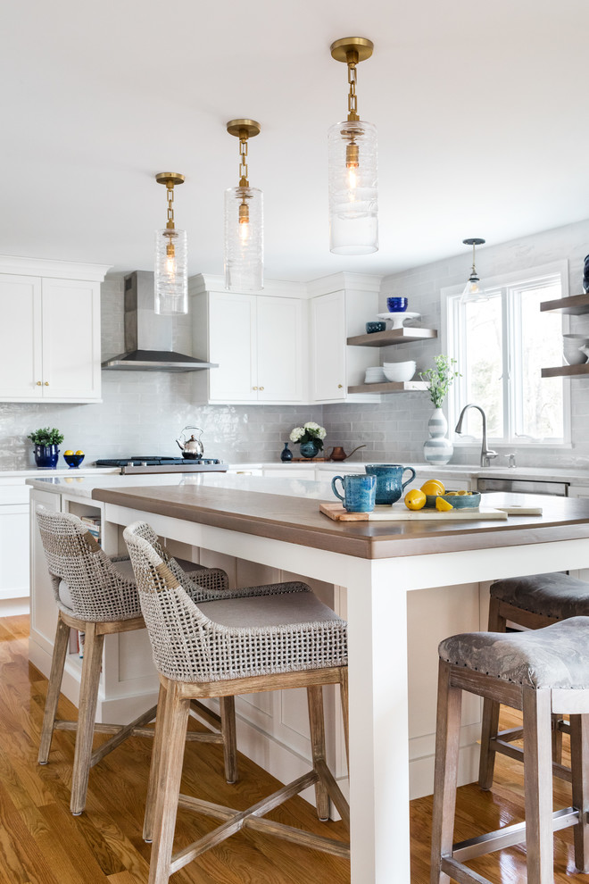 Beach style l-shaped eat-in kitchen in Boston with white cabinets, white splashback, stainless steel appliances, medium hardwood floors, with island, brown floor and white benchtop.
