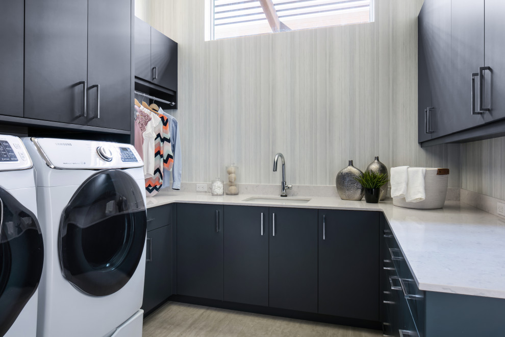 Inspiration for an expansive contemporary u-shaped dedicated laundry room in Tampa with an undermount sink, flat-panel cabinets, blue cabinets, quartz benchtops, white splashback, engineered quartz splashback, grey walls, porcelain floors, a side-by-side washer and dryer, grey floor, white benchtop and wallpaper.