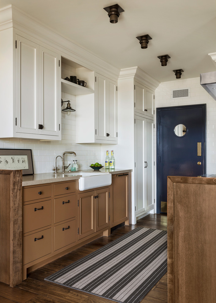 This is an example of a small traditional galley kitchen in Los Angeles with a farmhouse sink, recessed-panel cabinets, brown cabinets, white splashback, subway tile splashback, dark hardwood floors and no island.