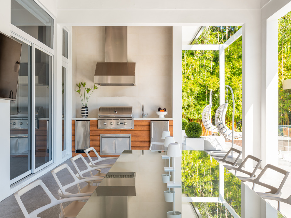 Cette photo montre un grand porche d'entrée de maison arrière tendance avec une cuisine d'été, une dalle de béton, une extension de toiture et un garde-corps en verre.
