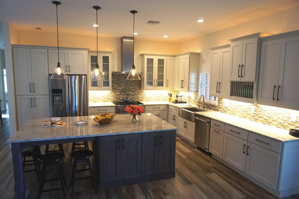 Inspiration for a mid-sized transitional l-shaped separate kitchen in Miami with a farmhouse sink, shaker cabinets, white cabinets, marble benchtops, beige splashback, matchstick tile splashback, stainless steel appliances, medium hardwood floors, with island and brown floor.