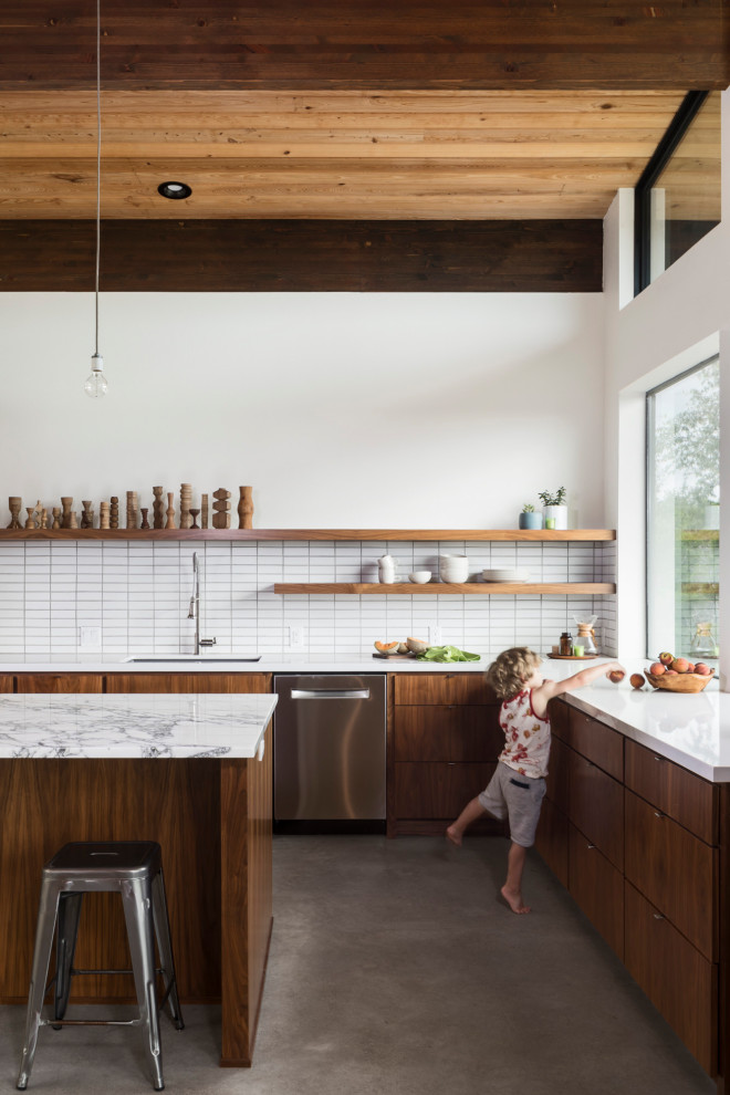 Inspiration for a midcentury l-shaped kitchen in Austin with flat-panel cabinets, medium wood cabinets, with island, an undermount sink, white splashback, stainless steel appliances, concrete floors, grey floor and white benchtop.