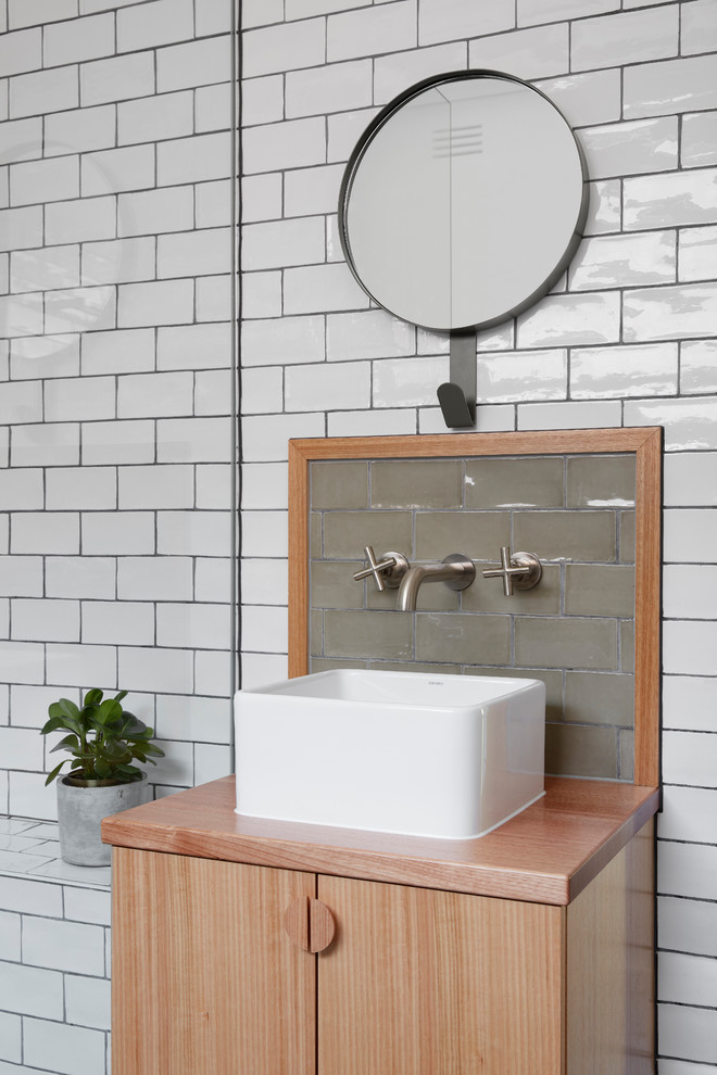 Inspiration for a small contemporary master bathroom in Melbourne with flat-panel cabinets, light wood cabinets, a corner tub, a shower/bathtub combo, subway tile, an integrated sink and wood benchtops.