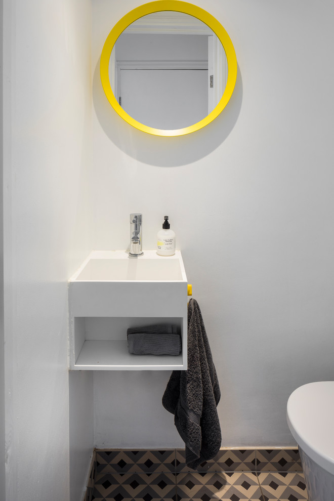 Photo of a small contemporary powder room in London with open cabinets, white cabinets, a wall-mount toilet, white walls, porcelain floors, an integrated sink and grey floor.