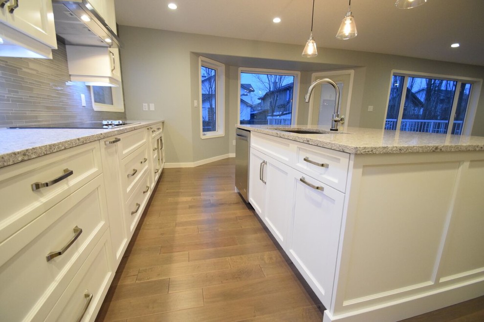 Eat-in kitchen - transitional l-shaped vinyl floor eat-in kitchen idea in Edmonton with a double-bowl sink, shaker cabinets, white cabinets, quartz countertops, gray backsplash, glass tile backsplash, stainless steel appliances and an island
