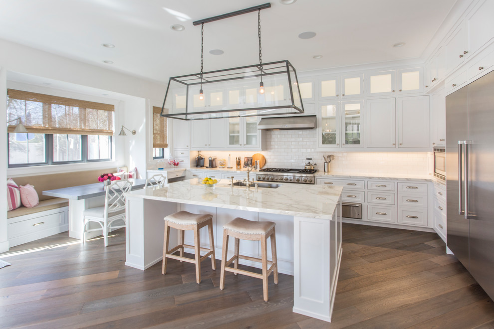 This is an example of a beach style l-shaped eat-in kitchen in Los Angeles with white splashback, stainless steel appliances, medium hardwood floors, with island, brown floor, an undermount sink, shaker cabinets, white cabinets and subway tile splashback.