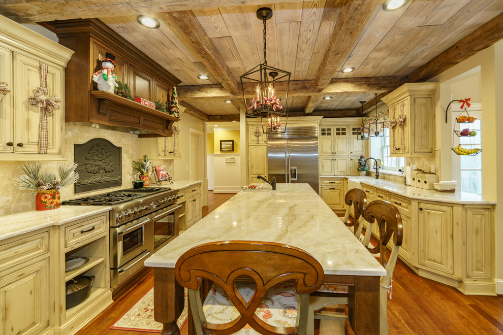Design ideas for a large country l-shaped eat-in kitchen in Bridgeport with a farmhouse sink, beaded inset cabinets, yellow cabinets, quartzite benchtops, beige splashback, marble splashback, stainless steel appliances, medium hardwood floors, multiple islands and beige benchtop.