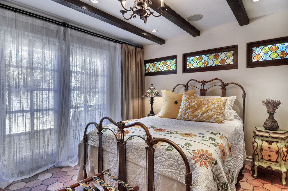 Photo of a mid-sized mediterranean guest bedroom in Orange County with white walls, terra-cotta floors, a standard fireplace and a stone fireplace surround.