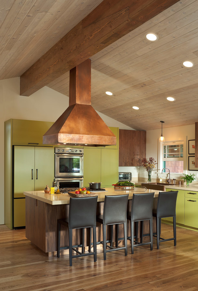 Inspiration for a mid-sized traditional u-shaped eat-in kitchen in San Francisco with a farmhouse sink, flat-panel cabinets, green cabinets, stainless steel appliances, with island and light hardwood floors.