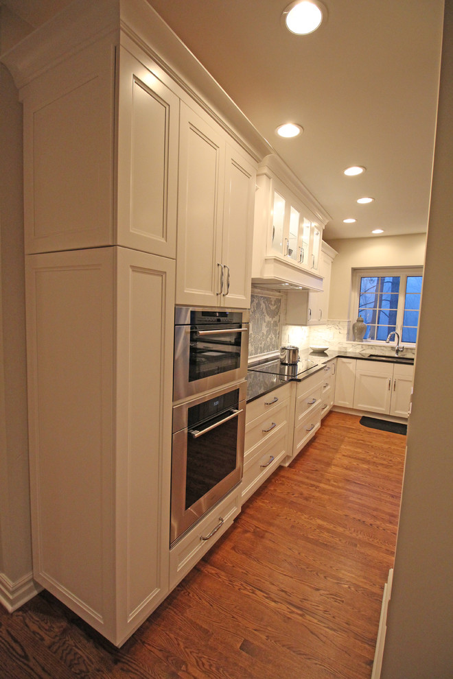 Mid-sized traditional u-shaped eat-in kitchen in Detroit with an undermount sink, recessed-panel cabinets, white cabinets, granite benchtops, grey splashback, mosaic tile splashback, panelled appliances, medium hardwood floors and with island.