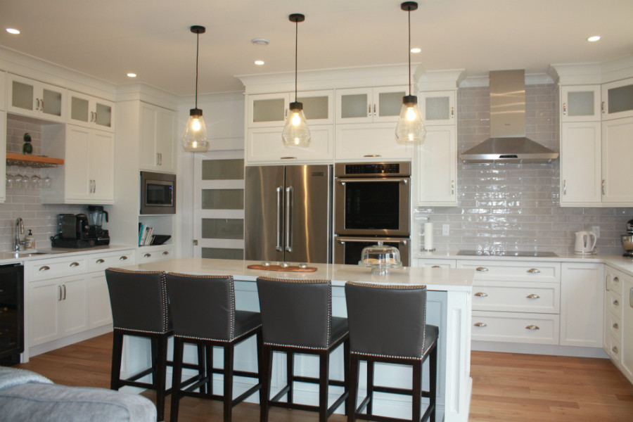 Example of a mid-sized transitional l-shaped medium tone wood floor kitchen pantry design with an undermount sink, shaker cabinets, white cabinets, quartz countertops, gray backsplash, cement tile backsplash, stainless steel appliances, an island and white countertops