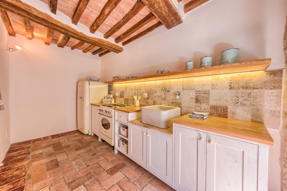 Design ideas for a small mediterranean single-wall separate kitchen in Other with a farmhouse sink, shaker cabinets, white cabinets, wood benchtops, beige splashback, ceramic splashback, terra-cotta floors and no island.