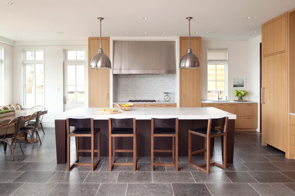 Transitional l-shaped eat-in kitchen in Minneapolis with flat-panel cabinets, light wood cabinets, white splashback, stone tile splashback, panelled appliances, limestone floors and with island.