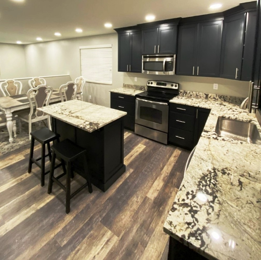 Inspiration for a mid-sized traditional l-shaped eat-in kitchen in Salt Lake City with a single-bowl sink, recessed-panel cabinets, black cabinets, granite benchtops, multi-coloured splashback, stone slab splashback, stainless steel appliances, vinyl floors, with island, grey floor and multi-coloured benchtop.