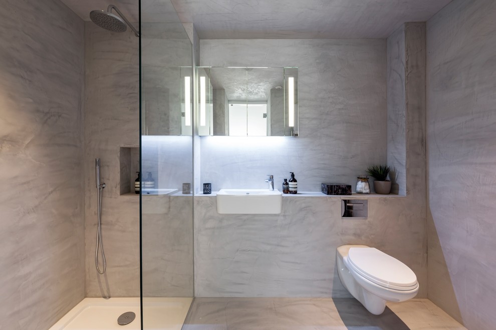 This is an example of a mid-sized contemporary 3/4 bathroom in London with an open shower, a wall-mount toilet, gray tile, grey floor, an open shower, grey walls and a wall-mount sink.