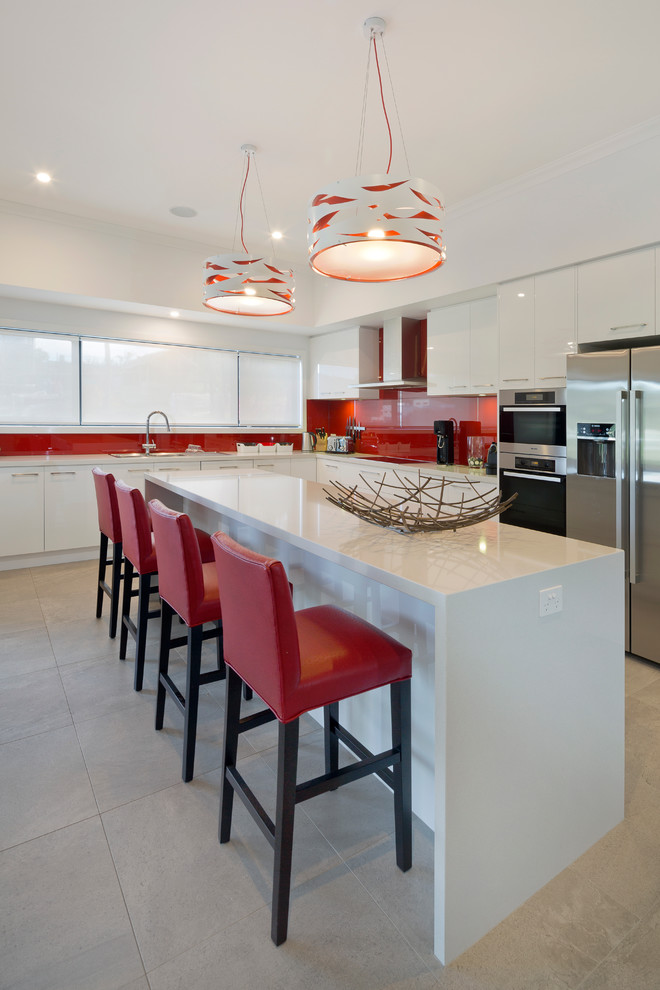 Inspiration for an expansive contemporary l-shaped open plan kitchen in Melbourne with an undermount sink, flat-panel cabinets, white cabinets, quartz benchtops, red splashback, glass sheet splashback, stainless steel appliances, ceramic floors and with island.