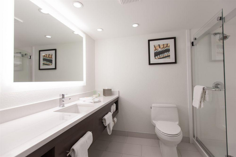Bild på ett stort funkis vit vitt badrum med dusch, med skåp i mörkt trä, en dusch i en alkov, en toalettstol med hel cisternkåpa, vita väggar, klinkergolv i keramik, ett nedsänkt handfat, vitt golv, dusch med skjutdörr och bänkskiva i akrylsten