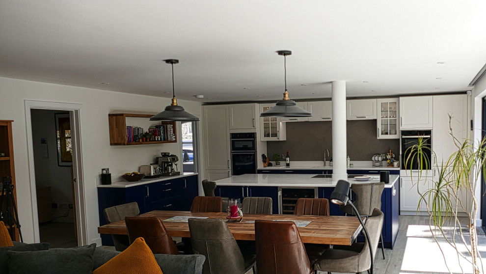Inredning av ett lantligt stort vit vitt kök, med en integrerad diskho, skåp i shakerstil, blå skåp, bänkskiva i koppar, grått stänkskydd, stänkskydd i travertin, svarta vitvaror, ljust trägolv, en köksö och beiget golv
