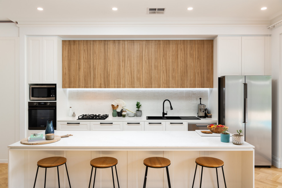 This is an example of a large contemporary kitchen in Adelaide with a double-bowl sink, shaker cabinets, white cabinets, quartz benchtops, white splashback, cement tile splashback, stainless steel appliances, light hardwood floors, with island, brown floor and white benchtop.